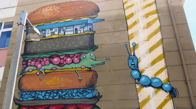 L’imperiese MrFijodor dipinge un hamburger gigante sulla facciata di una scuola per Athens Street Art Festival